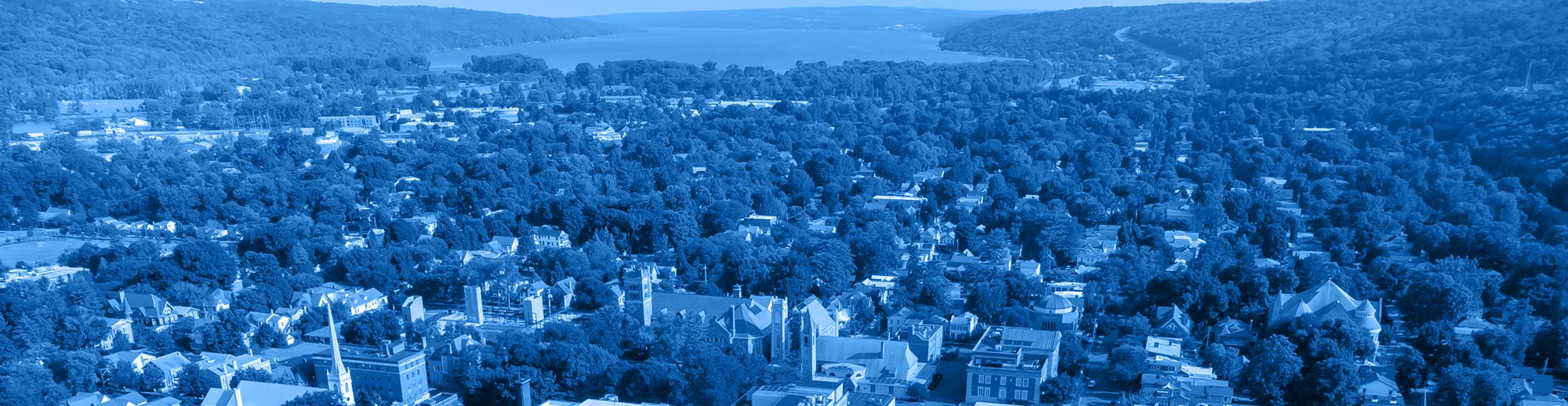 stock photo of ithaca new york view from high above with buildings and trees, cayuga lake in the background, all washed in monochromatic blue from the main logo